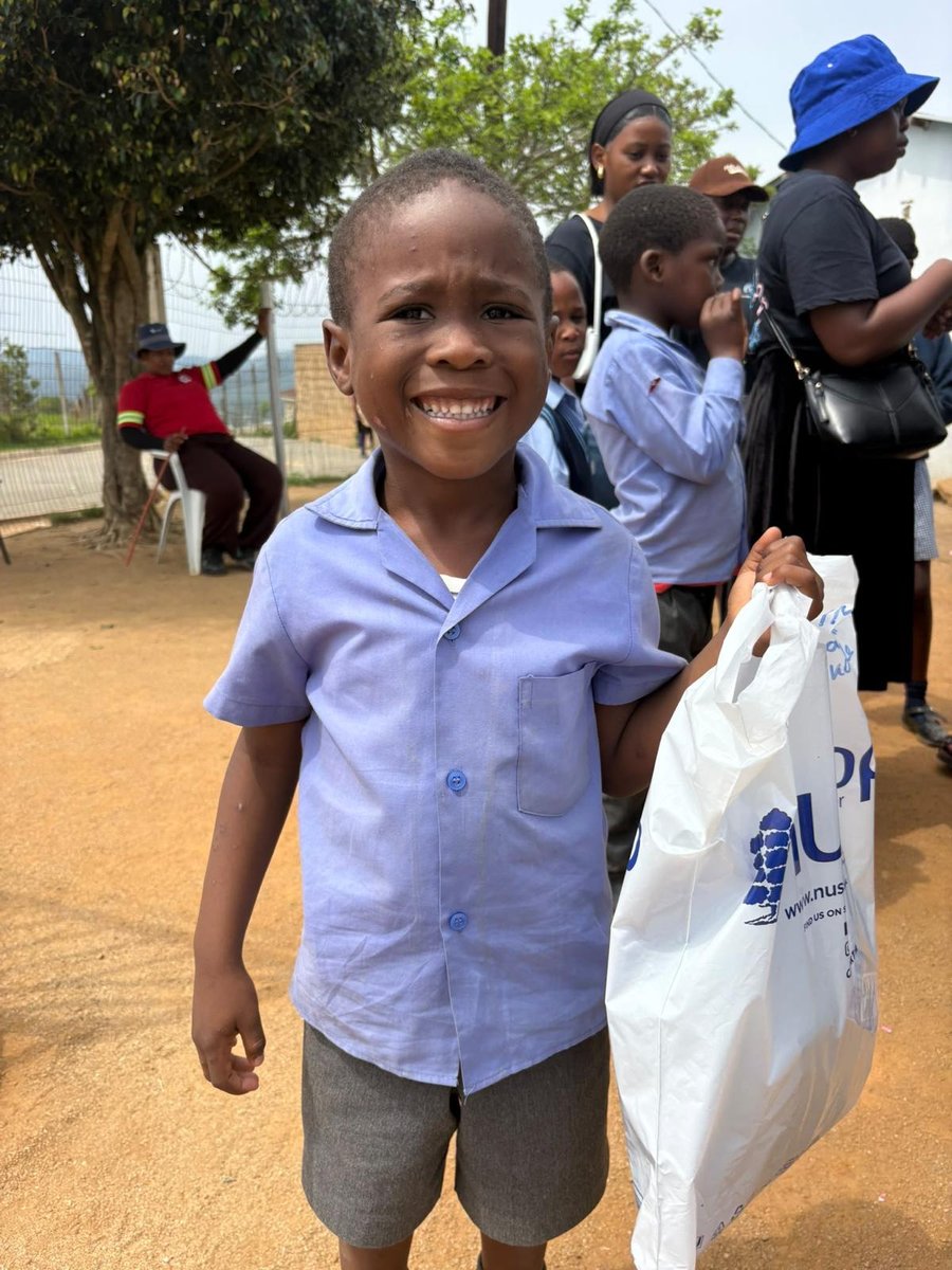 A smiling boy in his new school shirt and shorts, holding a Nushop bag