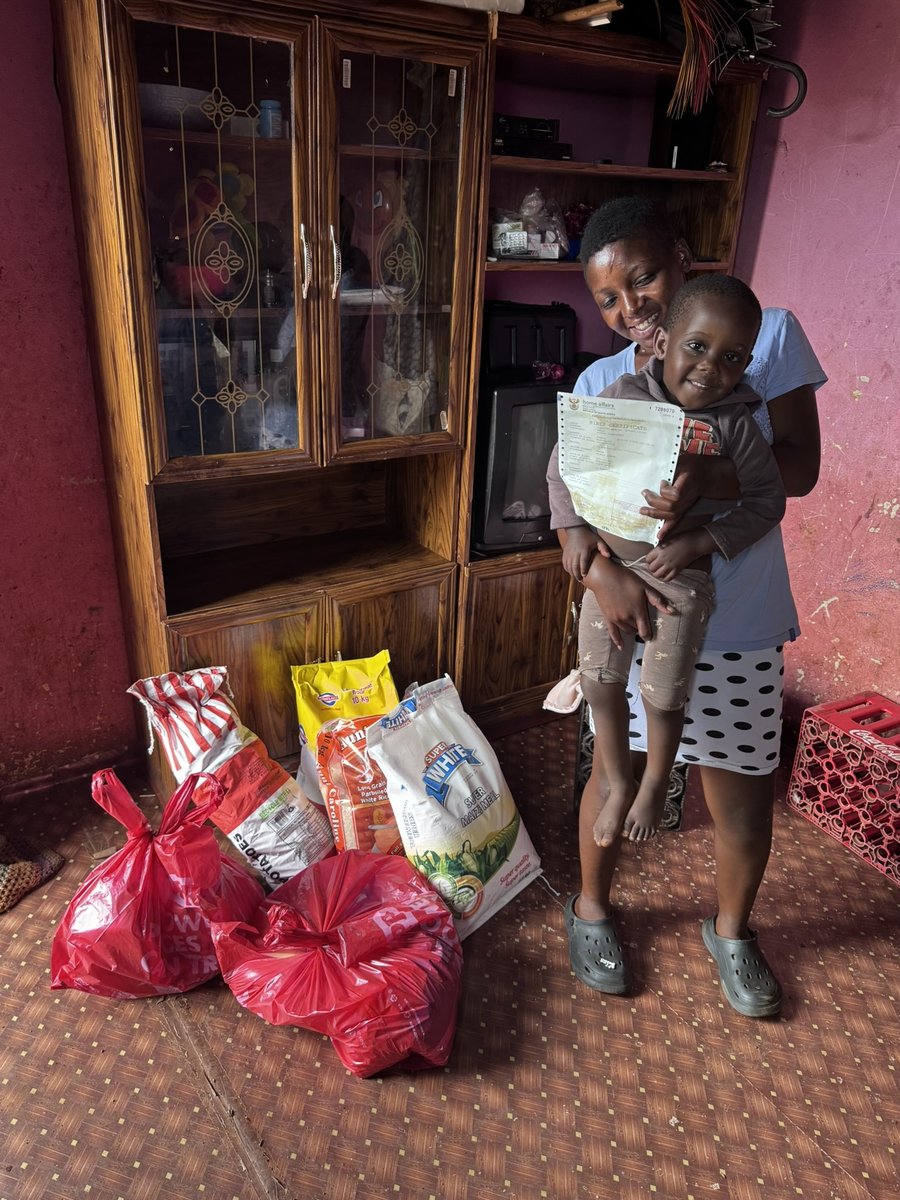 A mother holding her son's birth certificate, with a food parcel provided alongside