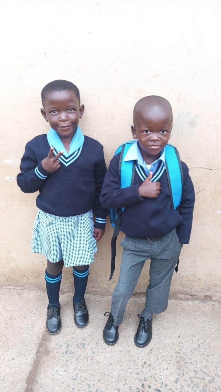 Two children in their new school uniforms, shoes and school bag