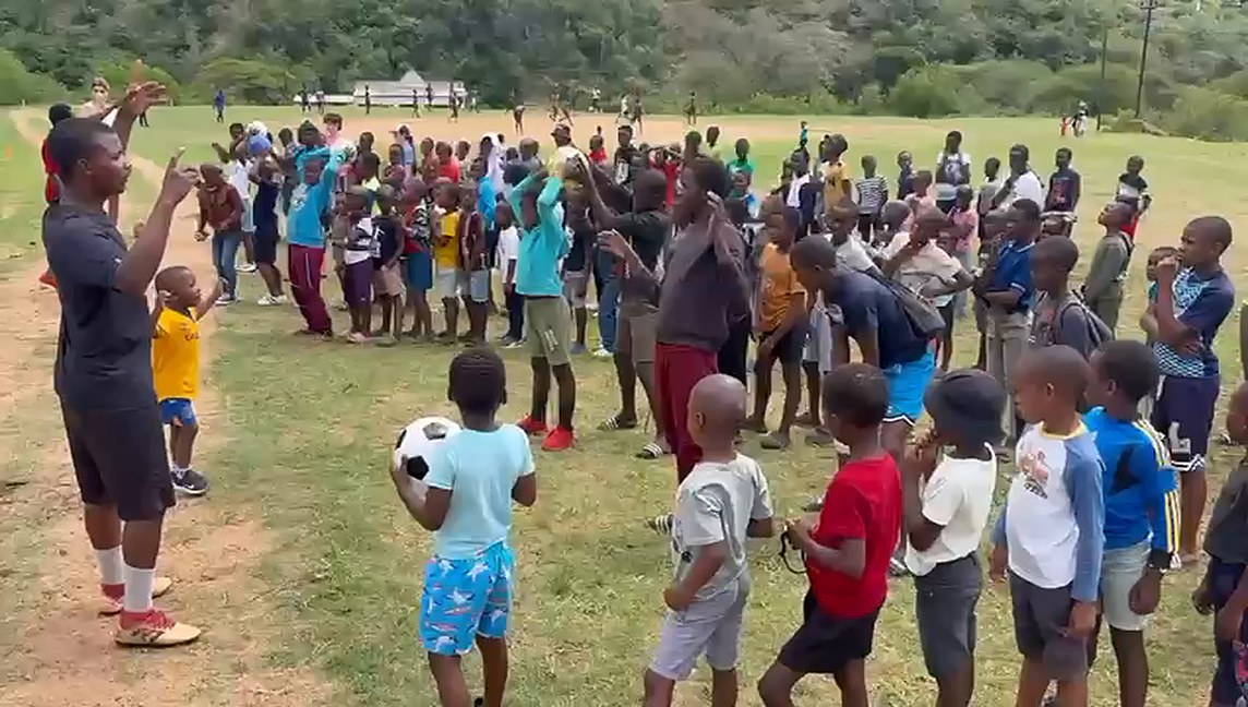 A coach and children holding footballs at a community sports day