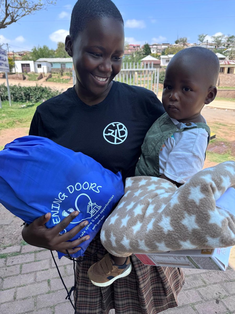 A young mum smiling at her baby, holding an Opening Doors bag and a blanket