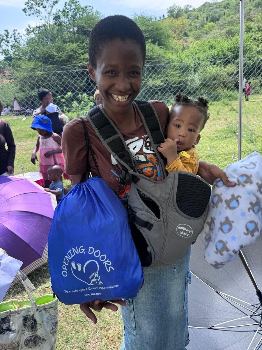 A smiling young mum carrying her baby, with an Opening Doors bag and a new blanket